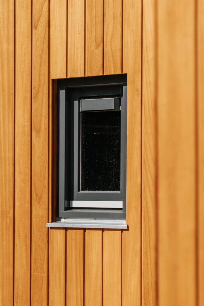 Thermo Ayous Fassadenverkleidung an modernem Wohnhaus — vertikale Holzbretter in warmem Goldbraun mit schwarzem Fensterrahmen
