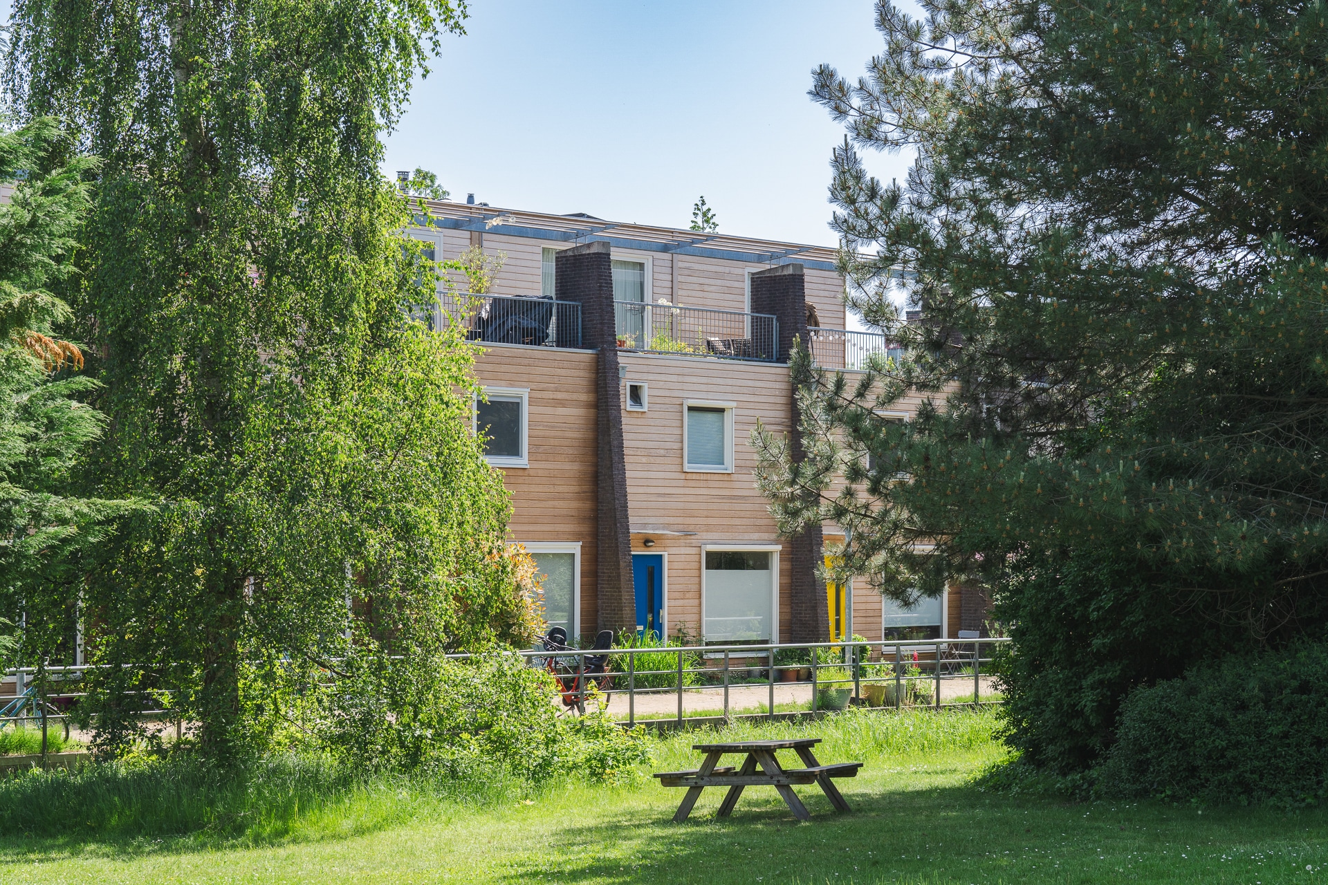 Gesamtansicht der Reihenhäuser mit Thermo-Fraké Fassade, umgeben von Bäumen, Grünflächen und einem Picknicktisch